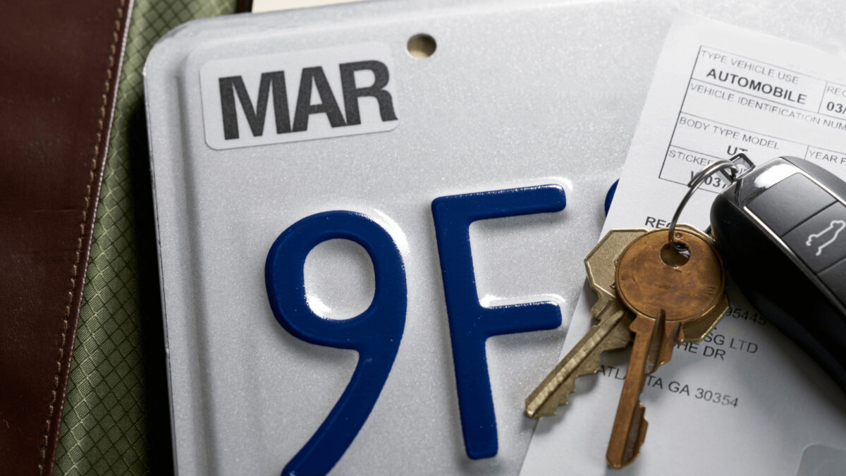 Close-up of California license plate with car keys on top, representing issues with vehicle title and registration delays in the state.